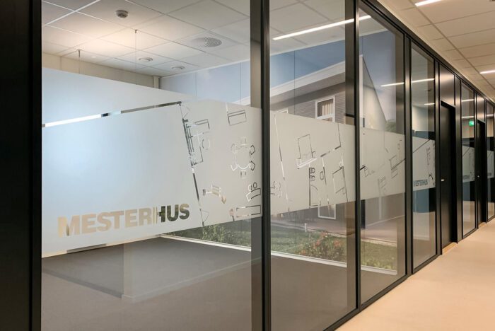 Glassvegg med frostet folie der plantegninger og Mesterhus-logoen er skåret ut.